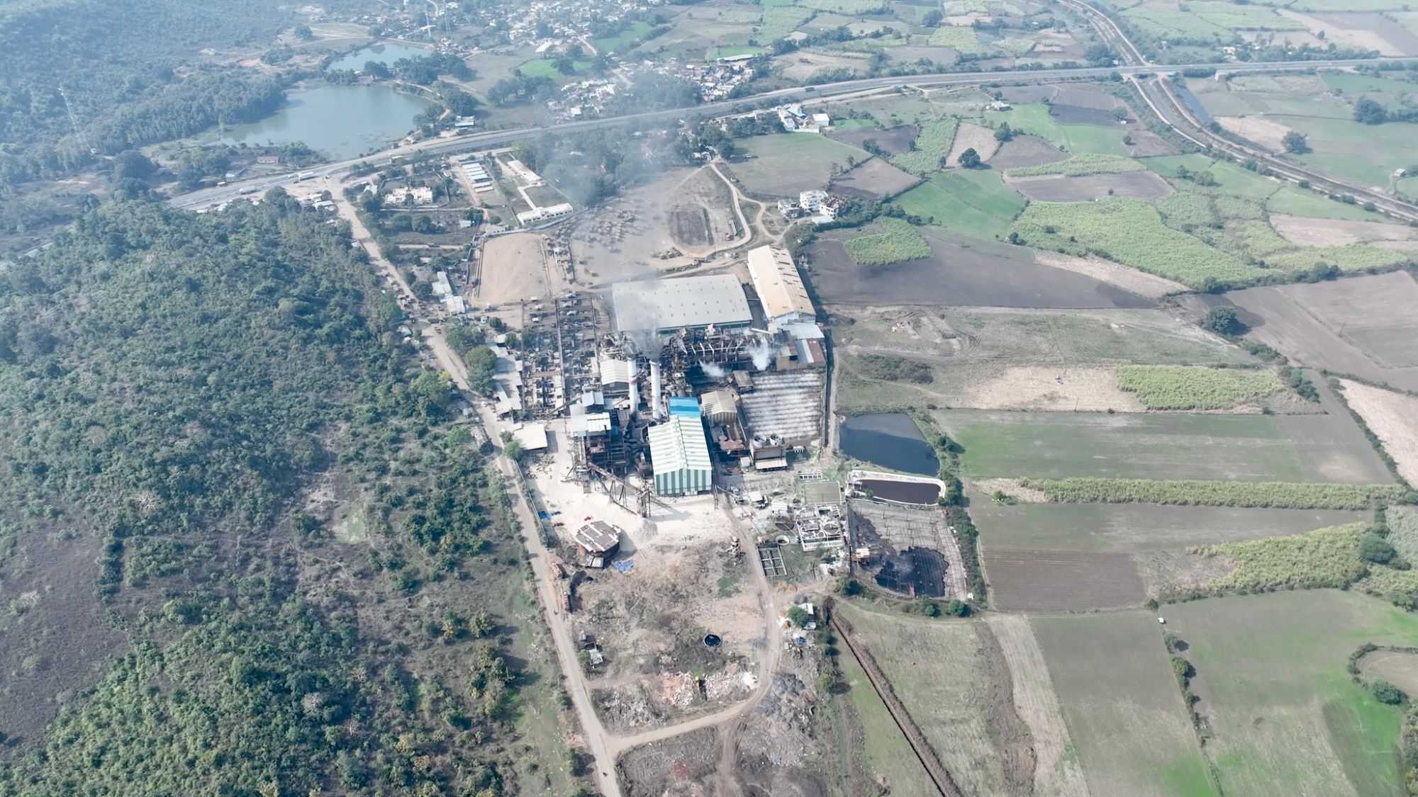 Aerial view of the whole complex at Bachai, Narsinghpur — the mill under steam, the distillery and the plant buildings, with cane and maize fields and the highway around them.
