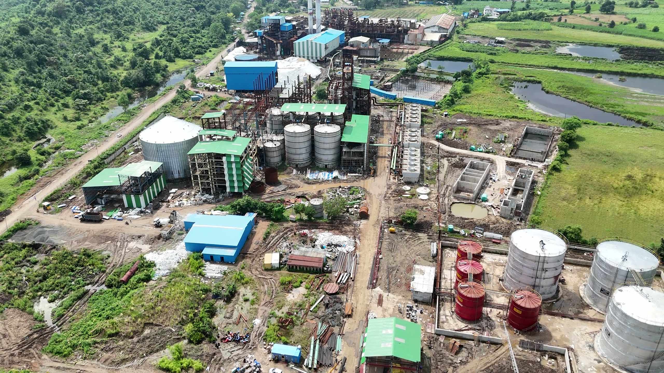 Aerial view of the whole complex at Bachai — the sugar mill sheds and boiler stack, the distillery house and columns, the storage silos and the ethanol tank farm, with the fields around the site.